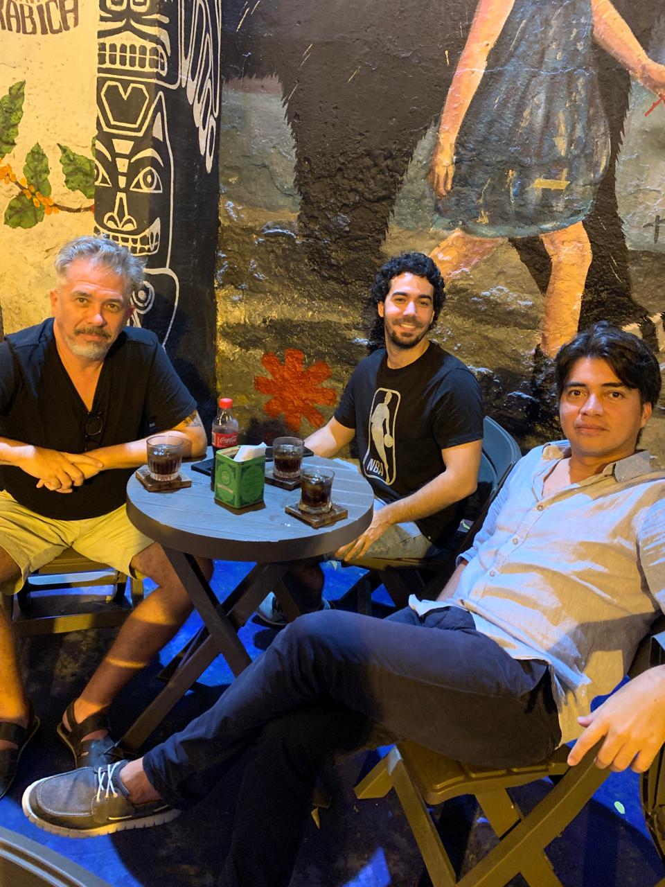 Tres personas disfrutando de una cata grupal de café frente a un mural con un tótem en el patio de Café del Mural.